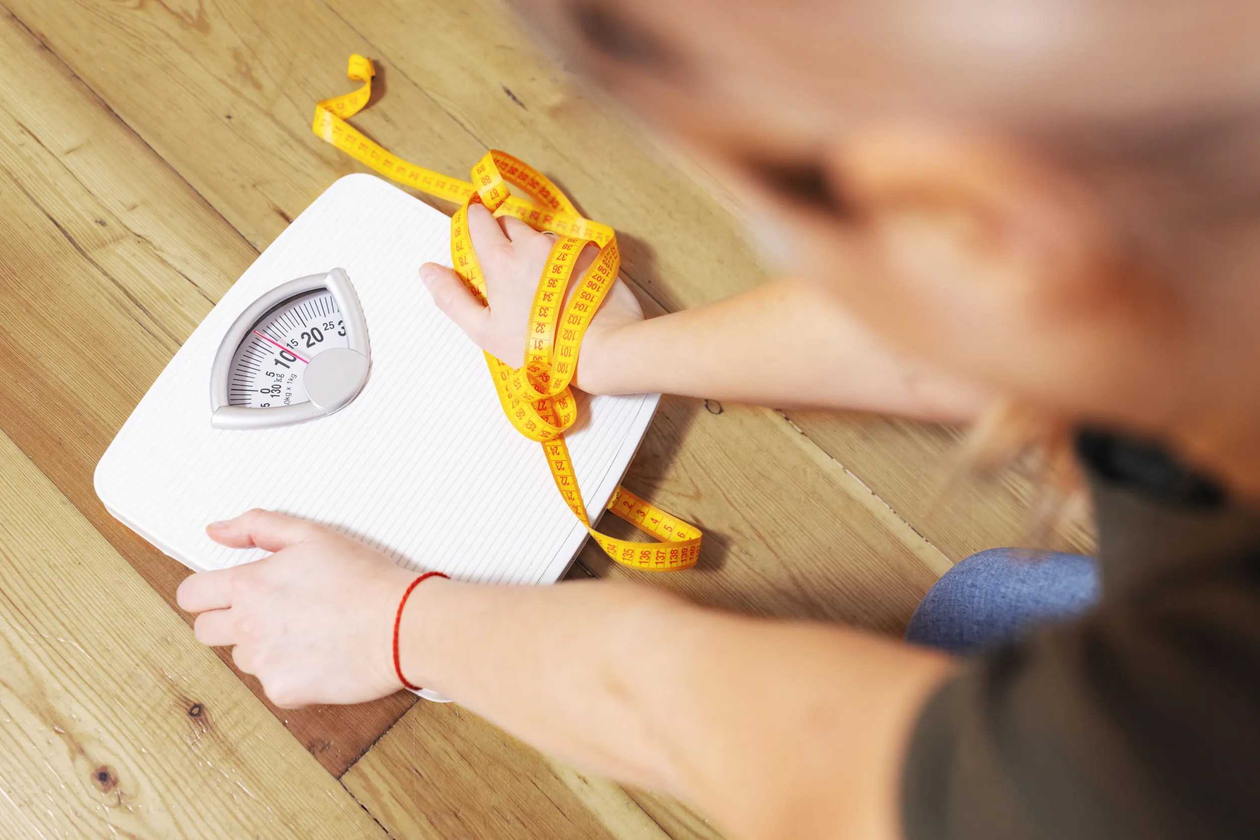 Depressed, frustrated and sad woman with a measuring tape looks at a white scale