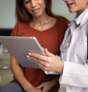 A healthcare professional in a white coat discusses information on a tablet with a patient in a medical setting A healthcare professional in a white coat discusses information on a tablet with a patient in a medical setting