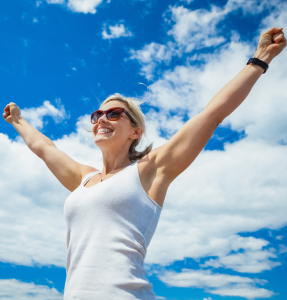 A woman stands joyfully with arms raised high against a bright blue sky filled with fluffy white clouds A woman stands joyfully with arms raised high against a bright blue sky filled with fluffy white clouds