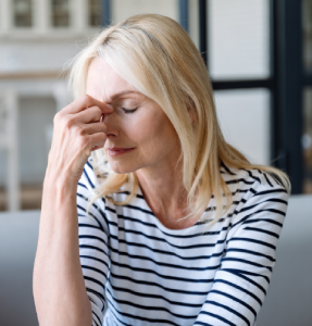 A woman with long blonde hair, wearing a striped shirt, rests her hand on her forehead, looking pensive in a cozy indoor setting A woman with long blonde hair, wearing a striped shirt, rests her hand on her forehead, looking pensive in a cozy indoor setting